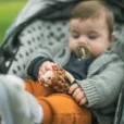 Baby in a stroller holding the Hedgehog HARRY rattle ring while using a pacifier