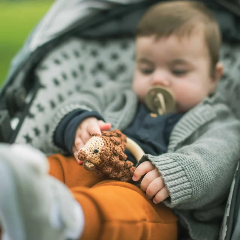 Rattle Ring Hedgehog HARRY – Use in Stroller Baby in a stroller holding the Hedgehog HARRY rattle ring while using a pacifier