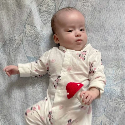 Babymädchen liegt auf gemusterter Decke und hält eine gehäkelte Fliegenpilz-Babyrassel