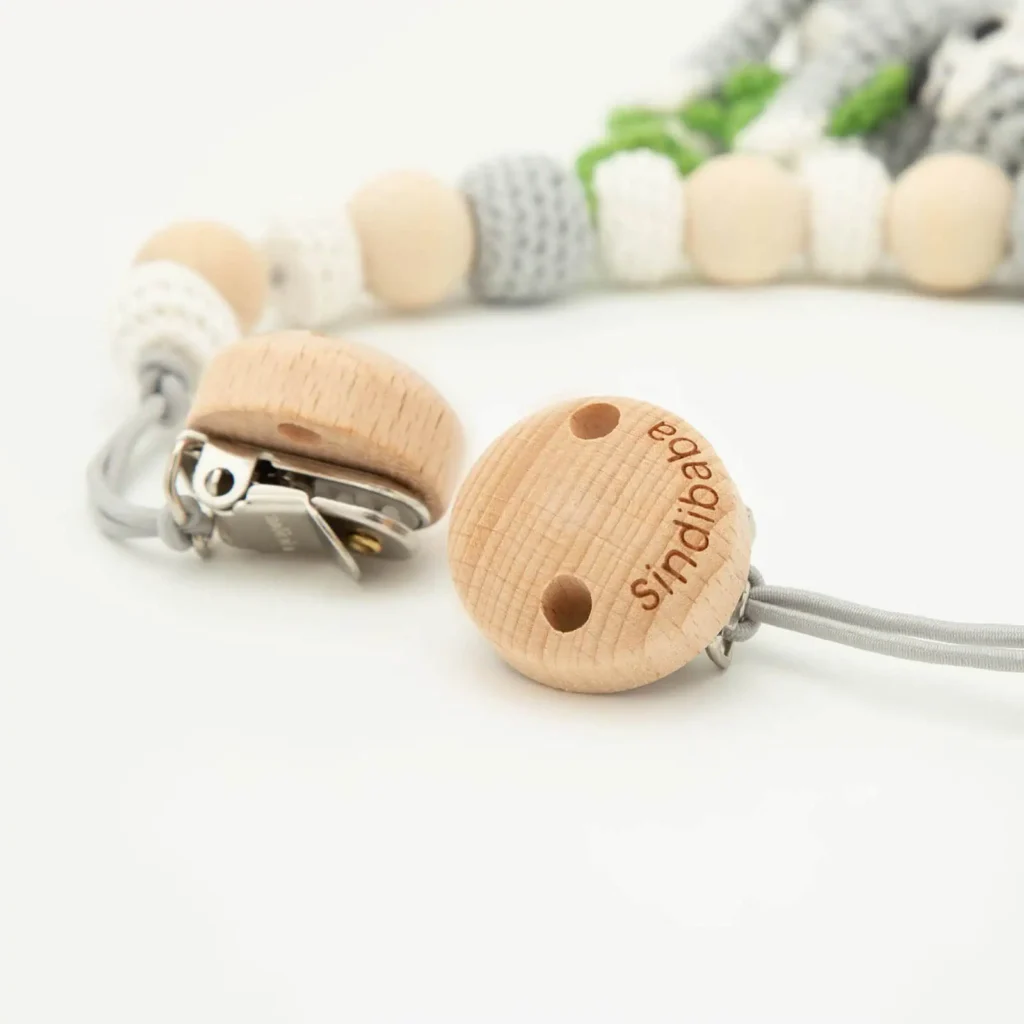 Detailaufnahme der Holzclips einer Kinderwagenkette mit Faultiermotiv, sichtbare Holzmaserung und Metallklemme, Perlen im Hintergrund unscharf
