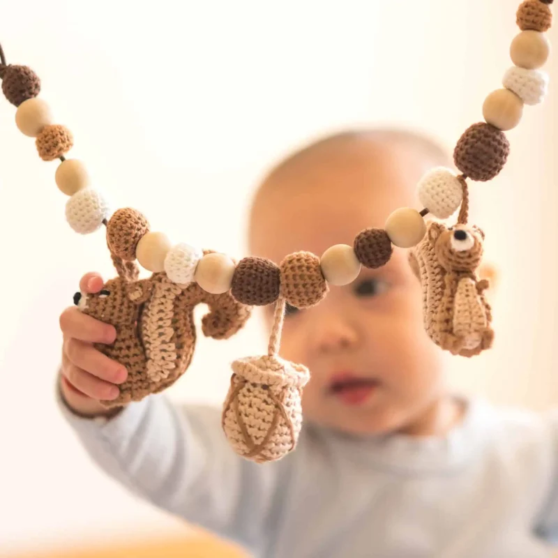 Lifestyle – Baby greift von unten Baby greift von unten nach dem gehäkelten Eichhörnchen der Kinderwagenkette.