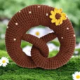 Gehäkelte Babyrassel Brezel mit Sonnenblume auf farbigem Hintergrund