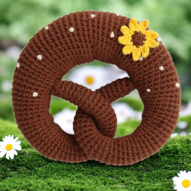 12628-baby-rattle-pretzel-sunflower-flatlay Gehäkelte Babyrassel Brezel mit Sonnenblume auf farbigem Hintergrund