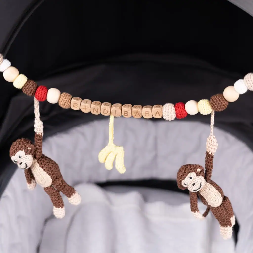 Personalisierte Kinderwagenkette Affe Charlie in Braun mit Markenname SINDIBABA – handgehäkeltes Babyspielzeug am Kinderwagen, detailreiche Aufnahme mit Holzclips und Naturmaterialien