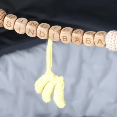 Detailaufnahme einer personalisierten Kinderwagenkette mit Wunschnamen und hängenden Bananen-Elementen.