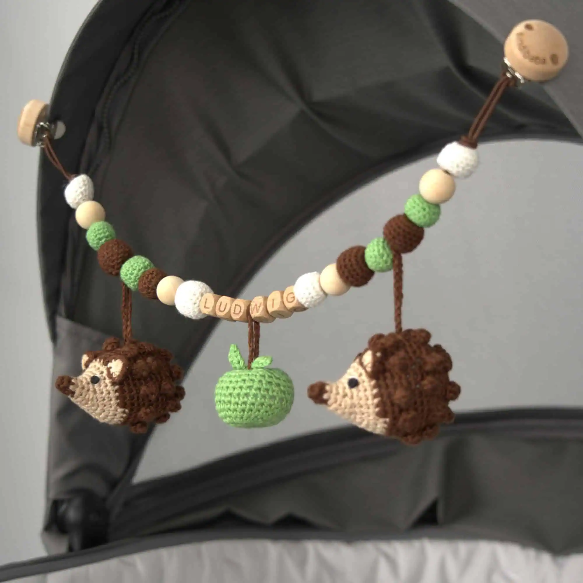 Personalisierte Kinderwagenkette mit Igel-Motiv und Namen Ludwig am Kinderwagen befestigt.