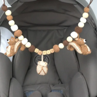 Personalisierte Kinderwagenkette mit Eichhörnchen-Motiv und Namen Janis am Maxi-Cosi befestigt.